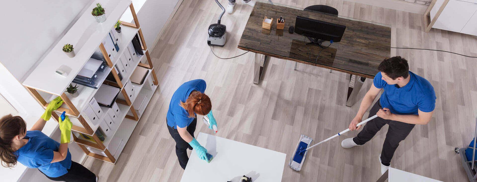 Three cleaners in blue uniforms cleaning a bright office