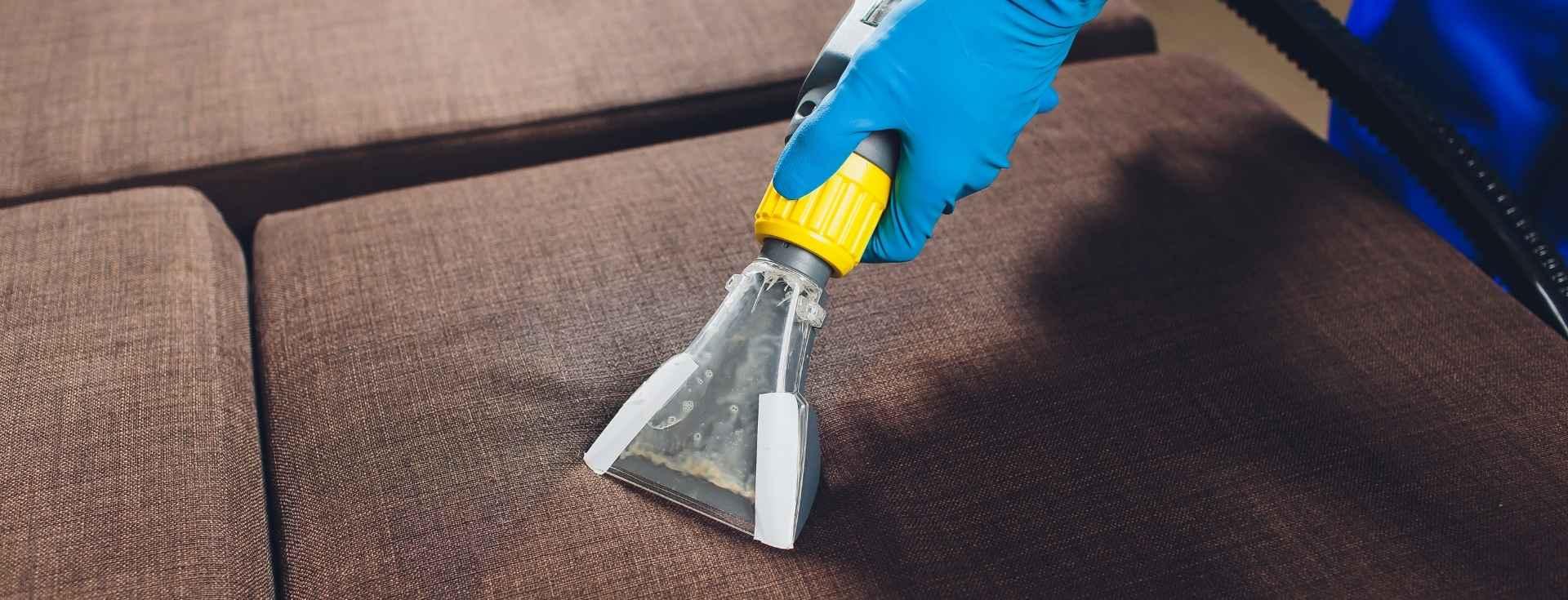 Gloved hand using an extraction tool on a brown fabric sofa